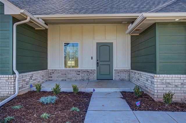 property entrance with roof with shingles and brick siding