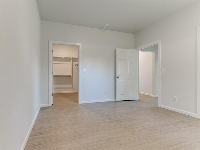 unfurnished bedroom with light wood-type flooring, a spacious closet, and a closet