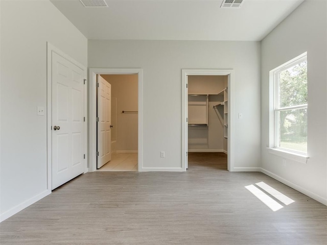 unfurnished bedroom with light hardwood / wood-style floors, a walk in closet, connected bathroom, and multiple windows