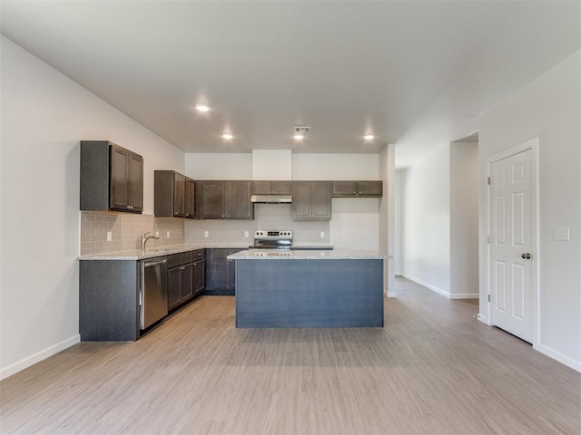 kitchen with light stone countertops, appliances with stainless steel finishes, backsplash, light hardwood / wood-style floors, and a kitchen island