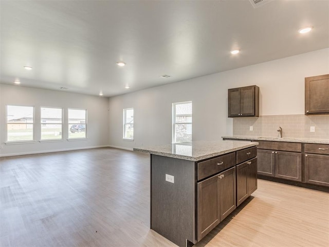 kitchen featuring a center island, light stone counters, backsplash, and light hardwood / wood-style flooring