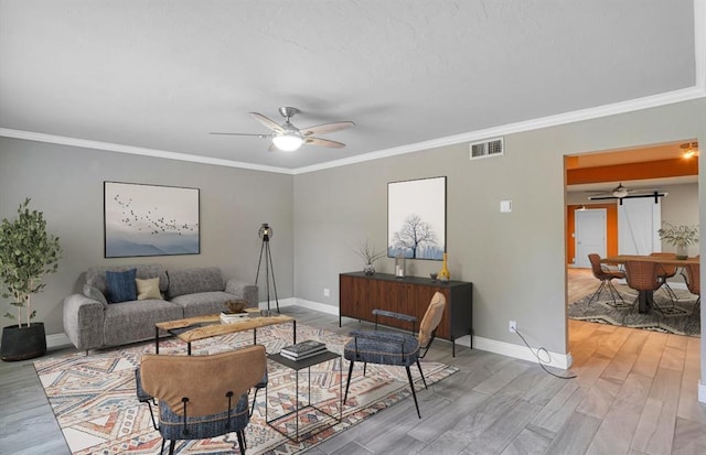 living room with light wood-type flooring, a barn door, ceiling fan, and crown molding