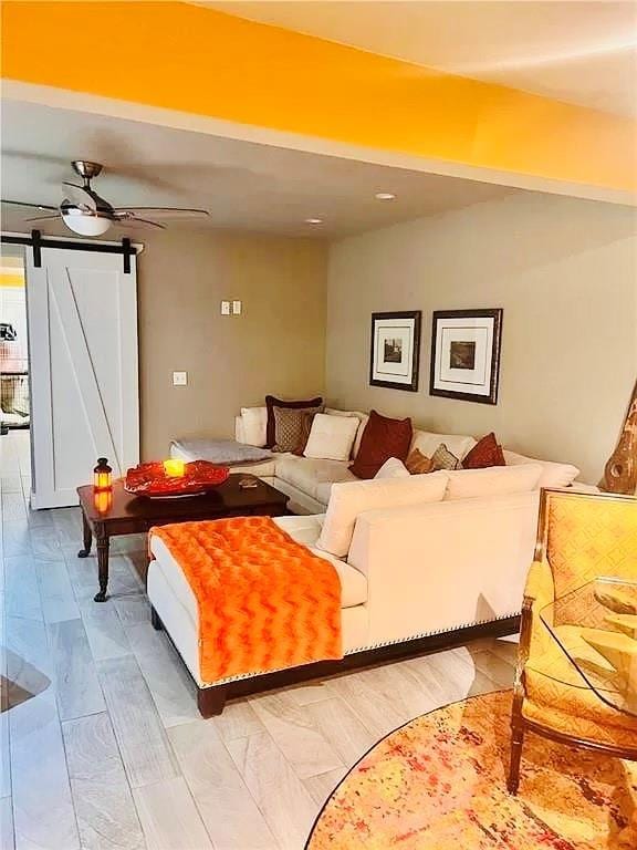 living room with light wood-type flooring, a barn door, and ceiling fan