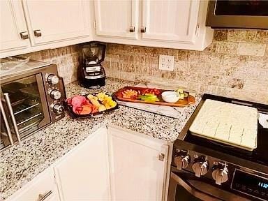 interior space with white cabinets, tasteful backsplash, light stone counters, and stainless steel range oven