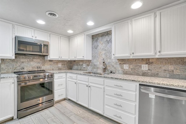 kitchen featuring appliances with stainless steel finishes, tasteful backsplash, light stone counters, sink, and white cabinetry