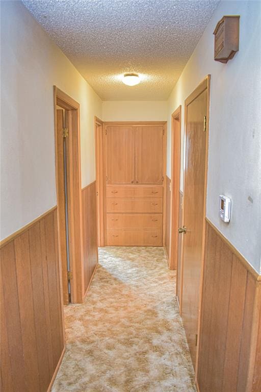 corridor with wood walls, light colored carpet, and a textured ceiling