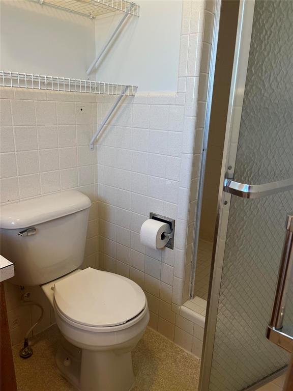 bathroom with an enclosed shower, vanity, toilet, and tile walls