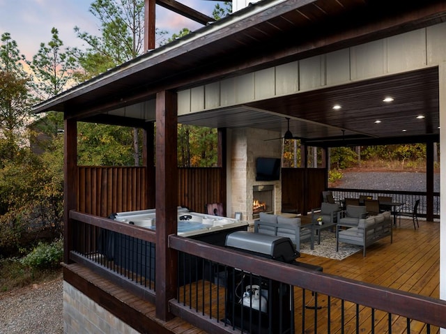 deck at dusk featuring ceiling fan, a hot tub, area for grilling, and an outdoor living space with a fireplace