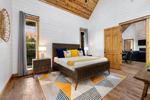 bedroom featuring wooden walls, light hardwood / wood-style floors, high vaulted ceiling, wooden ceiling, and a stone fireplace