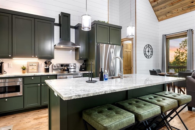 kitchen featuring stainless steel appliances, light stone countertops, pendant lighting, a kitchen bar, and wall chimney range hood