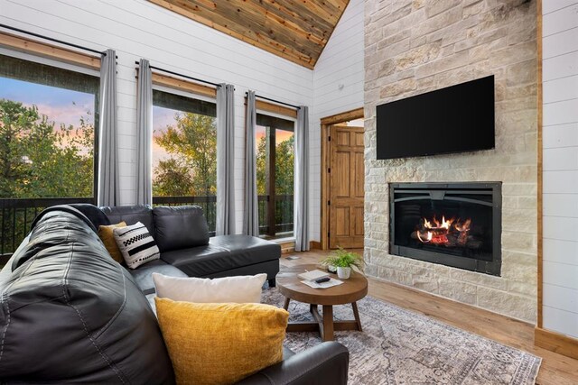 living room with high vaulted ceiling, a stone fireplace, wood walls, and wood-type flooring