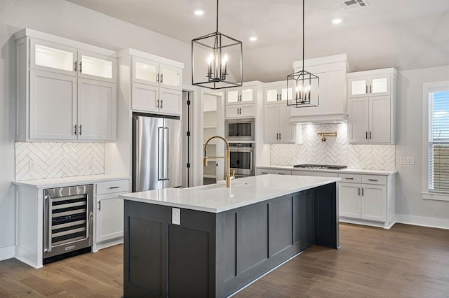 kitchen featuring appliances with stainless steel finishes, wine cooler, dark wood-type flooring, a center island with sink, and white cabinetry