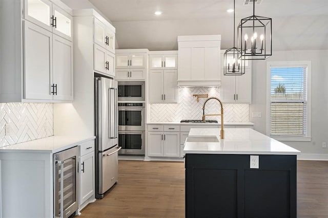 kitchen with white cabinets, appliances with stainless steel finishes, a center island with sink, and wine cooler