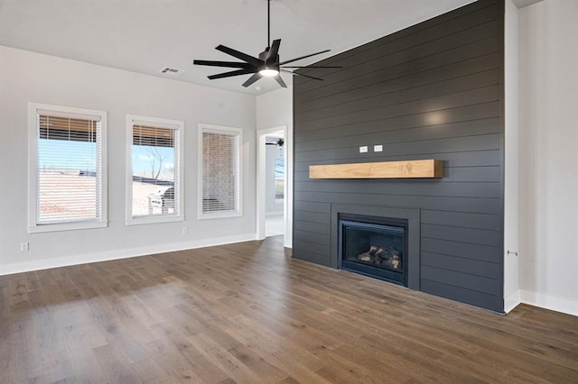 unfurnished living room with dark hardwood / wood-style floors, ceiling fan, a fireplace, and wooden walls