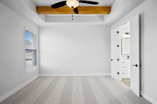 carpeted empty room with beam ceiling, a raised ceiling, and ceiling fan