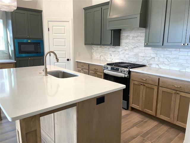 kitchen featuring light countertops, custom range hood, a kitchen island with sink, stainless steel gas stove, and a sink