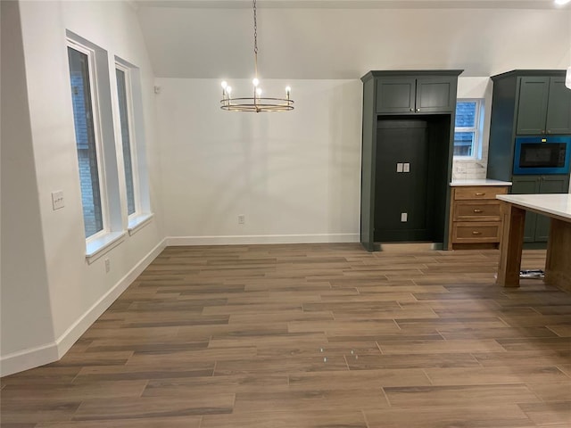 unfurnished dining area with a chandelier, lofted ceiling, dark wood-style flooring, baseboards, and plenty of natural light