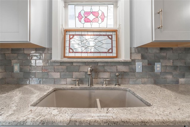 kitchen featuring white cabinets, backsplash, light stone countertops, and sink