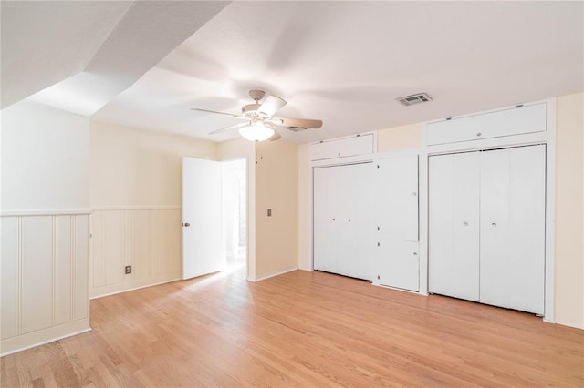 unfurnished bedroom with ceiling fan, light hardwood / wood-style flooring, and two closets