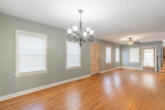 empty room with ceiling fan with notable chandelier, a textured ceiling, and light hardwood / wood-style flooring