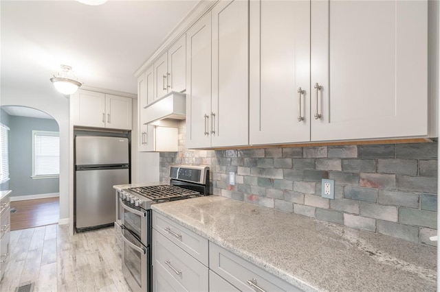 kitchen featuring white cabinetry, light hardwood / wood-style floors, appliances with stainless steel finishes, tasteful backsplash, and light stone counters