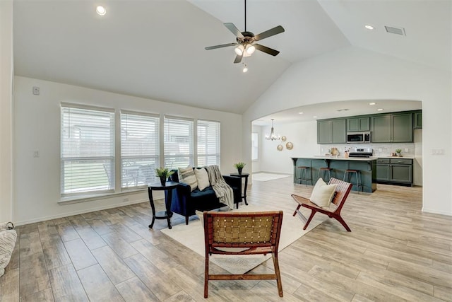 living room with ceiling fan with notable chandelier, high vaulted ceiling, and light hardwood / wood-style flooring