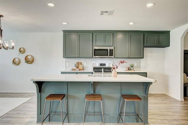 kitchen featuring backsplash, stainless steel appliances, pendant lighting, a center island with sink, and light hardwood / wood-style floors