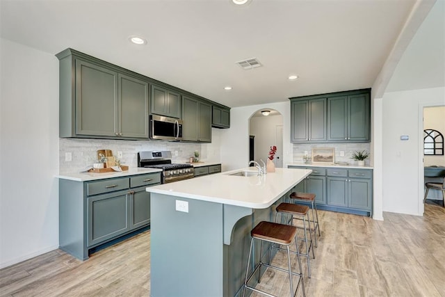 kitchen featuring sink, decorative backsplash, a kitchen island with sink, appliances with stainless steel finishes, and light wood-type flooring