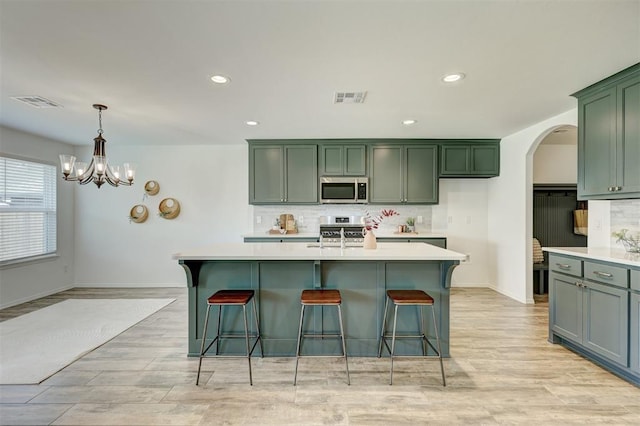 kitchen featuring pendant lighting, backsplash, a center island with sink, light hardwood / wood-style flooring, and stainless steel appliances