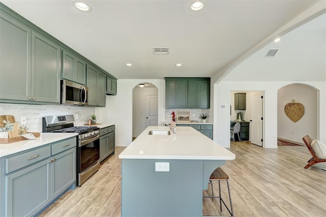 kitchen featuring sink, stainless steel appliances, tasteful backsplash, green cabinets, and light hardwood / wood-style flooring