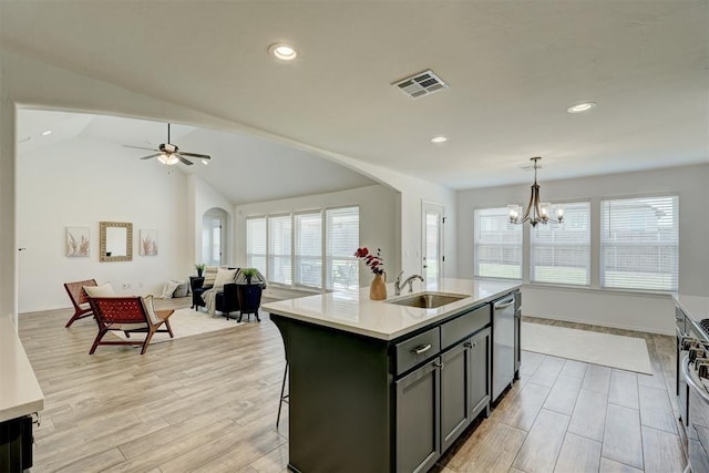 kitchen featuring sink, decorative light fixtures, light hardwood / wood-style flooring, lofted ceiling, and an island with sink