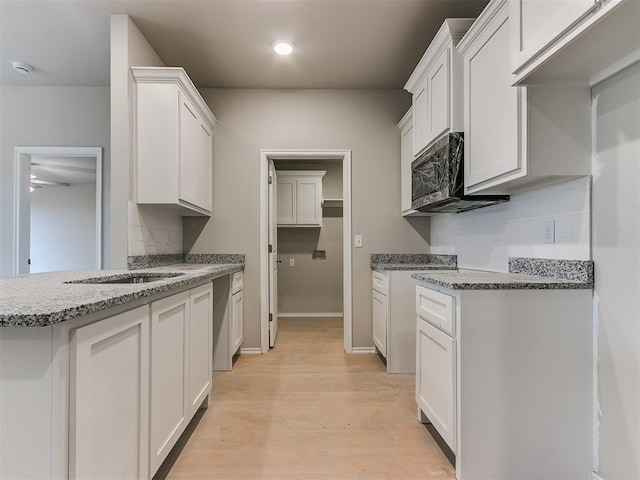 kitchen with stone counters, tasteful backsplash, light wood-style flooring, white cabinetry, and baseboards