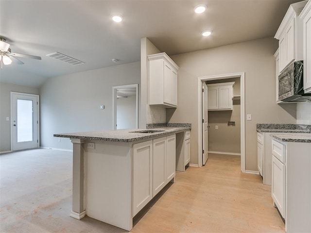 kitchen featuring a peninsula, light stone countertops, visible vents, and white cabinets