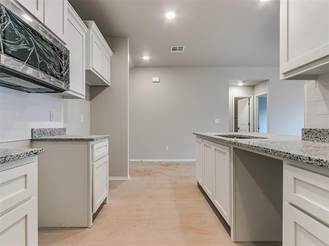 kitchen with tasteful backsplash, visible vents, light stone counters, and stainless steel microwave