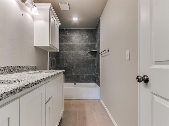 bathroom with wood finished floors, visible vents, vanity, baseboards, and washtub / shower combination