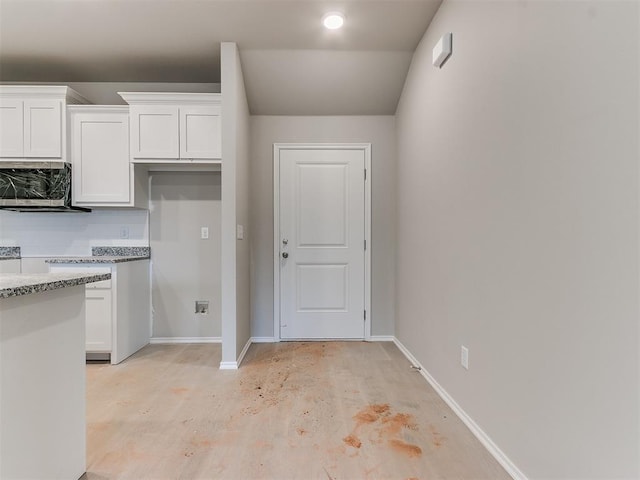 kitchen featuring baseboards, concrete floors, white cabinetry, and decorative backsplash