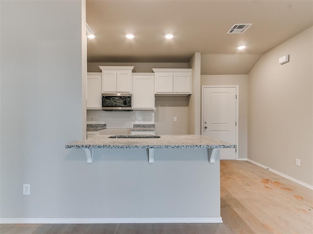 kitchen featuring light stone counters, stainless steel microwave, visible vents, white cabinets, and a kitchen bar