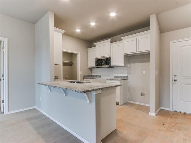 kitchen with stainless steel microwave, white cabinetry, light stone countertops, a peninsula, and a kitchen bar