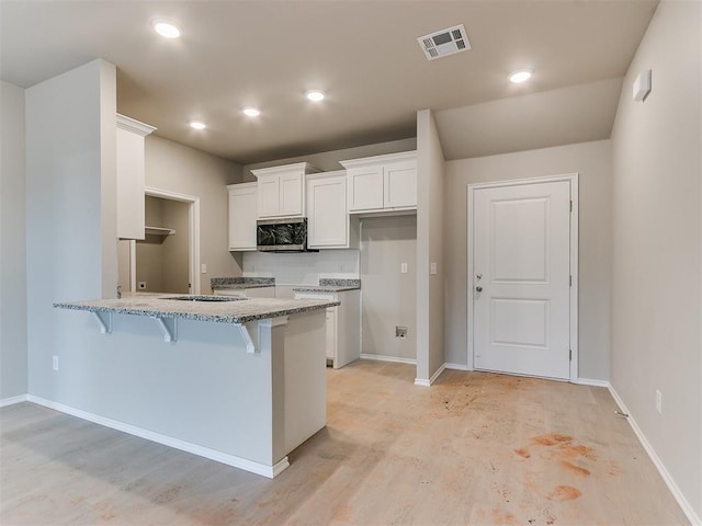 kitchen featuring a peninsula, a breakfast bar, white cabinetry, light stone countertops, and stainless steel microwave