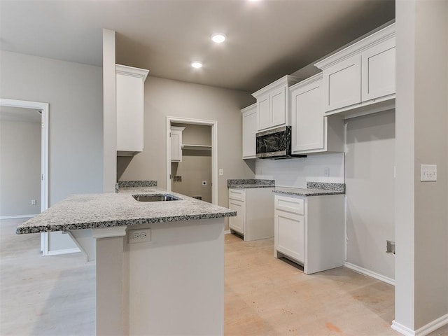 kitchen featuring light stone counters, a breakfast bar, stainless steel microwave, white cabinets, and a peninsula