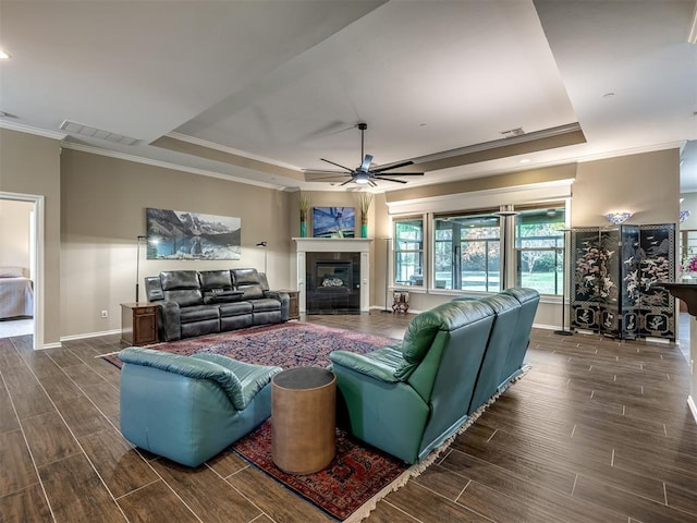 living area with wood finish floors, a fireplace, visible vents, a raised ceiling, and crown molding