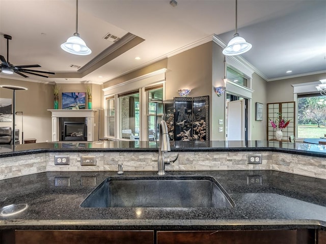 kitchen featuring visible vents, ornamental molding, a glass covered fireplace, a sink, and dark stone counters