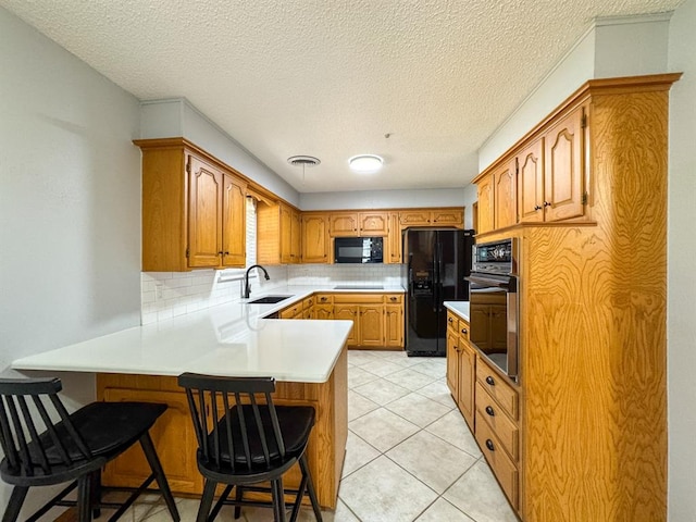 kitchen with black appliances, decorative backsplash, sink, and a breakfast bar area