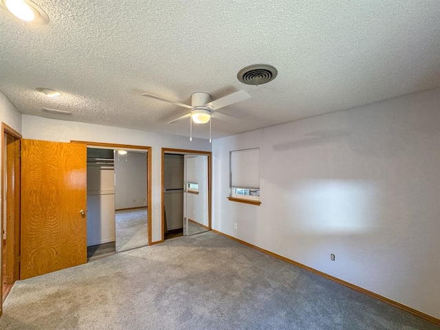 unfurnished bedroom with carpet flooring, multiple closets, ceiling fan, and a textured ceiling