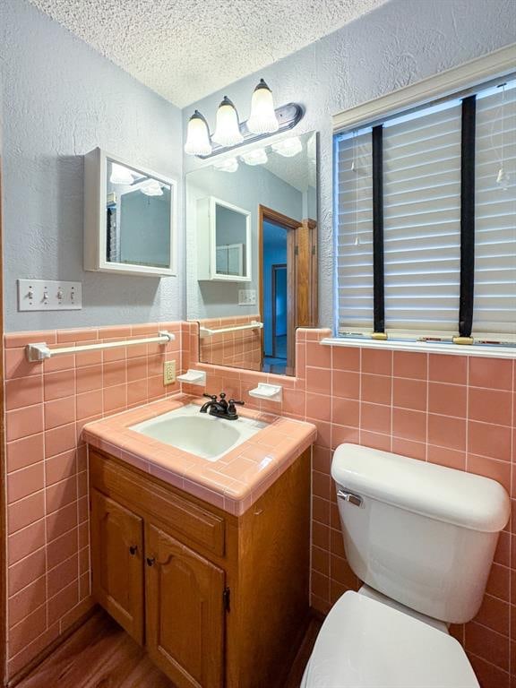 bathroom featuring vanity, a textured ceiling, toilet, and tile walls