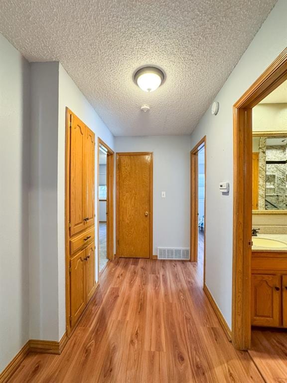 hallway with light hardwood / wood-style flooring, a textured ceiling, and sink