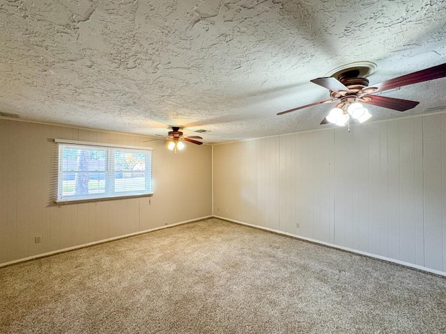 carpeted empty room with a textured ceiling, ceiling fan, and wood walls