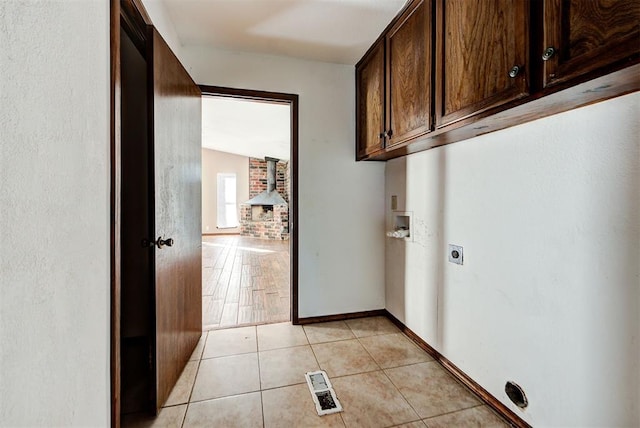 clothes washing area featuring a wood stove, cabinets, hookup for an electric dryer, hookup for a washing machine, and light tile patterned floors