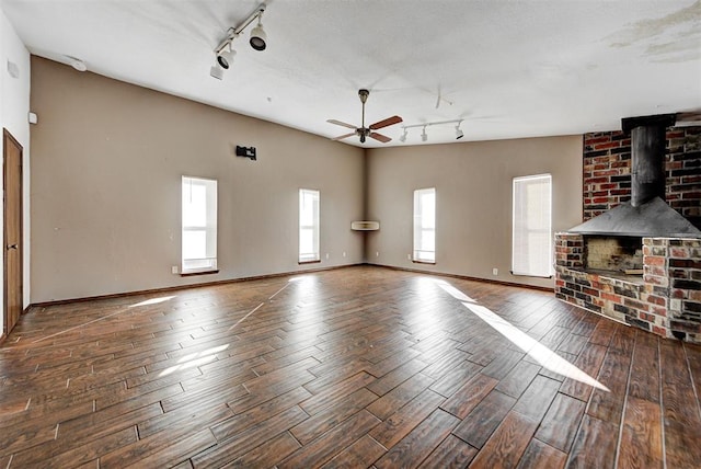 unfurnished living room with dark hardwood / wood-style flooring, track lighting, a wood stove, and ceiling fan