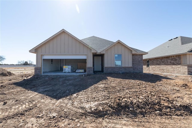 view of front of house featuring brick siding, roof with shingles, dirt driveway, an attached garage, and board and batten siding